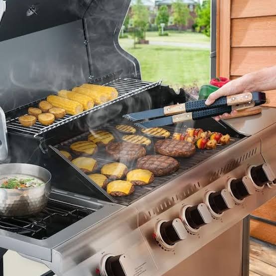 Burgers, corn and kebabs cooking on a stainless gas grill